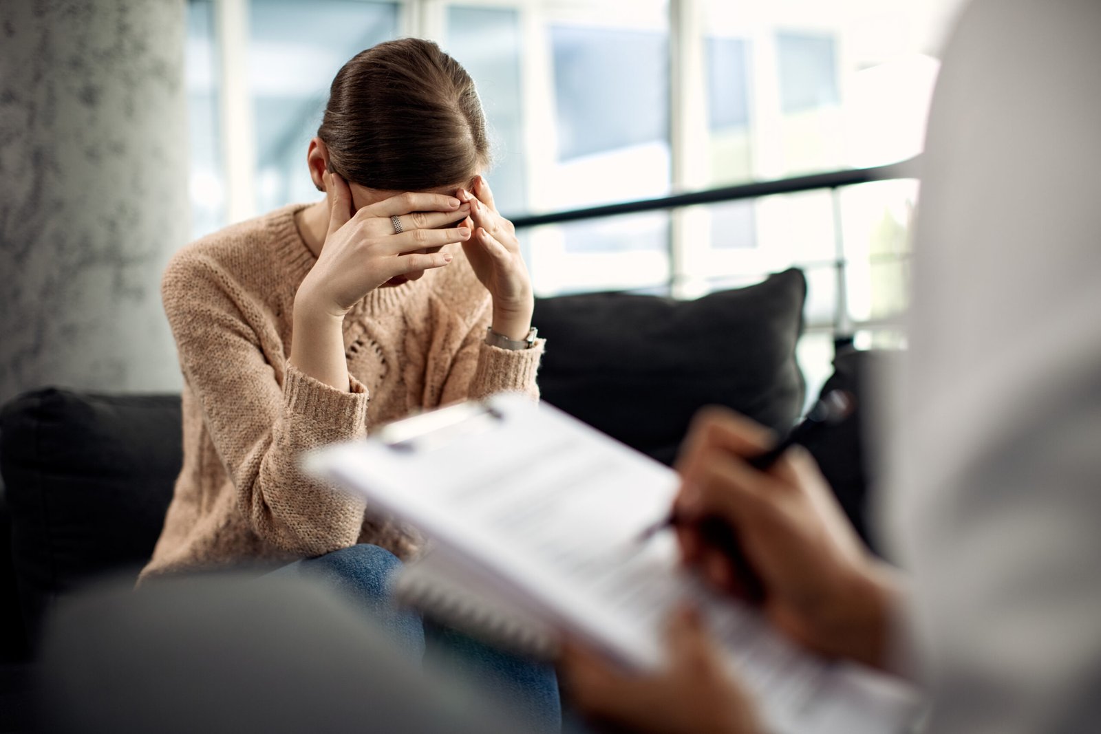 Sad woman holding her head in pain while having a meeting with psychotherapist.