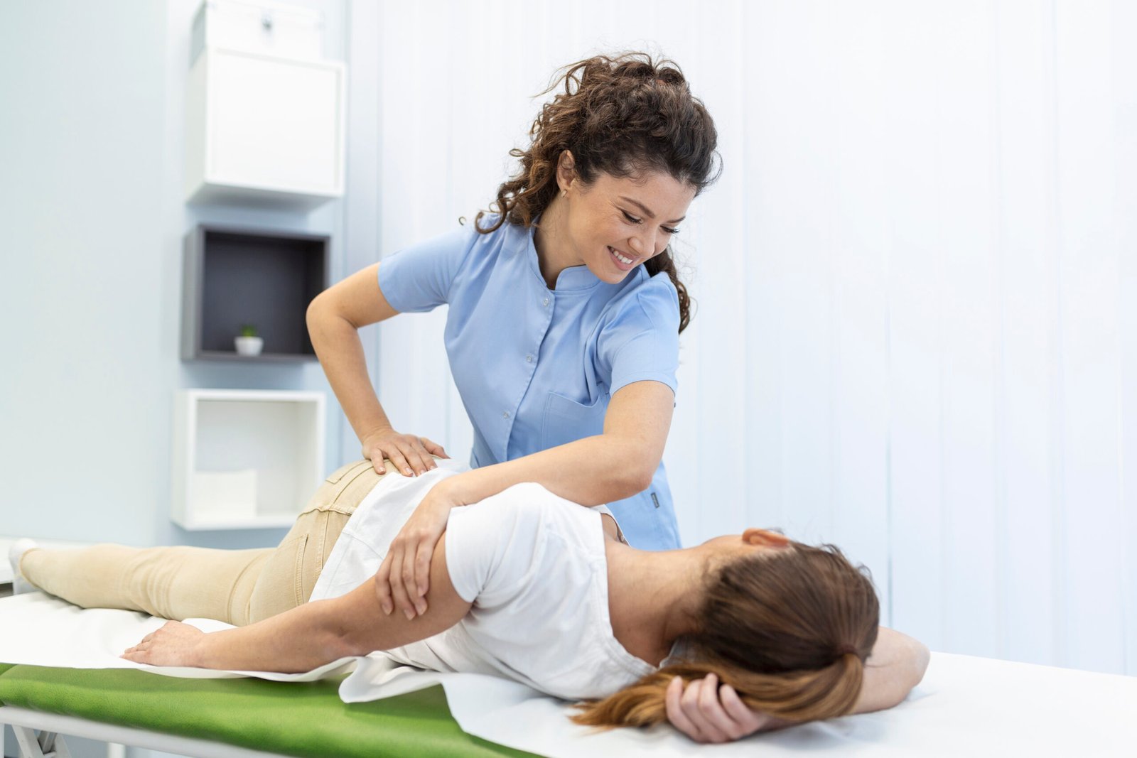 Young woman doctor chiropractor or osteopath fixing lying womans back with hands movements during visit in manual therapy clinic. Professional chiropractor during work